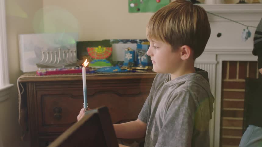 A young boy carries a candelabra to a windowsill