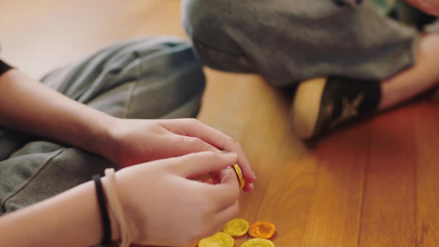 Mother and daughter laugh as they sit on floor playing game and girl eats one of chocolate pieces