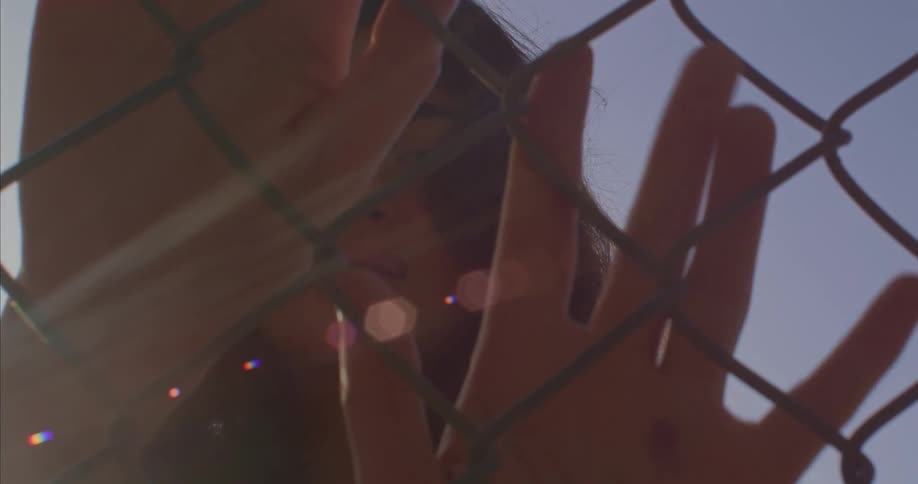 A teenage girl standing behind a chain link fence with her hands up