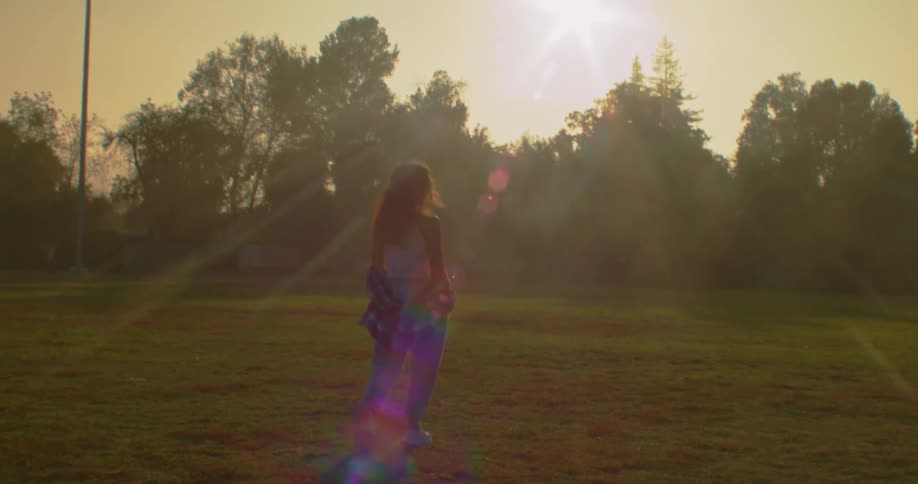 Young woman walking on the park turns around to look at the camera at sunset