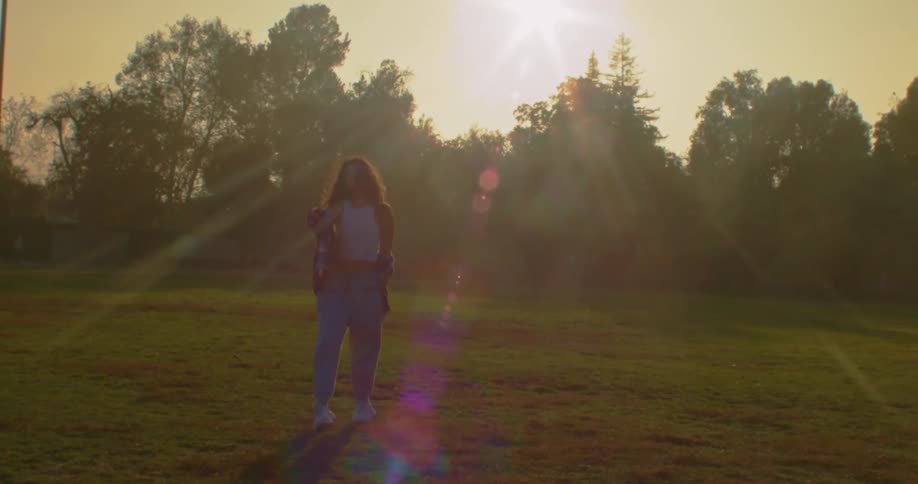 Young woman on a park at sunset walking backwards looking at the camera
