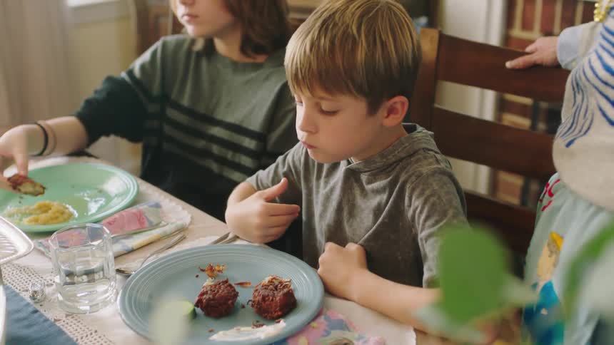 Two boys sit at a dinner table eating food