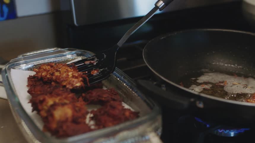 A woman uses a spatula to remove a potato latke from the cooking oil