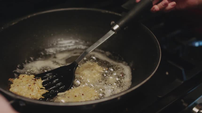 A woman flips food in oil in a frying pan as she cooks at home