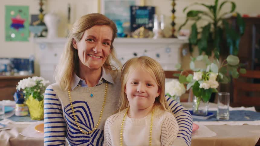 Mother holds daughter on her lap as they pose near a dining table