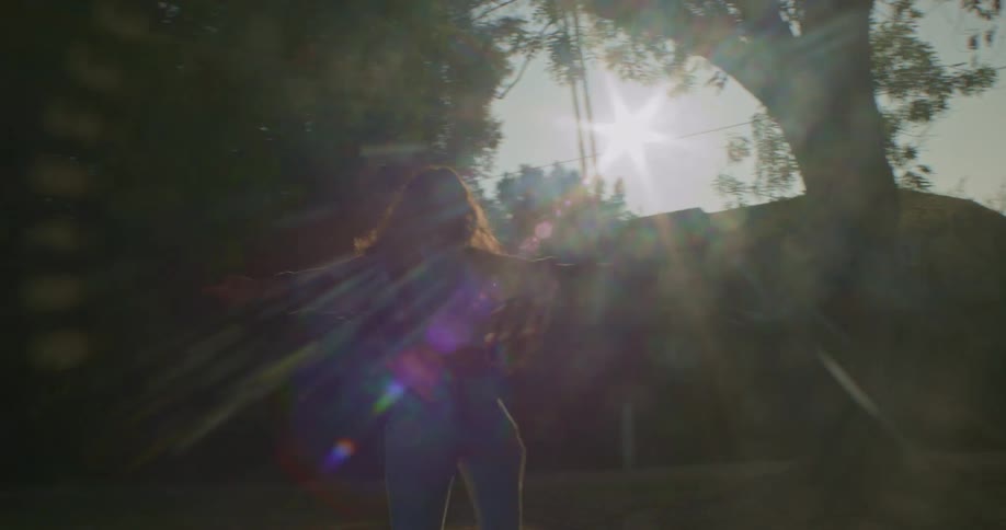 Young girl spinning with arms wide open on a park at sunset
