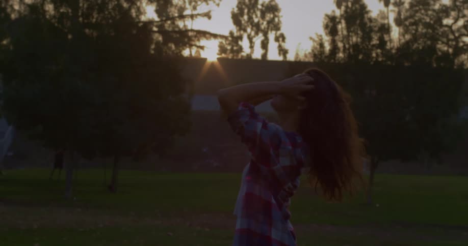 A teenager pulls her hair up while standing in a park