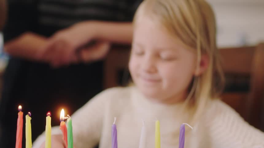 Girl sits in chair lighting birthday candles and smiling