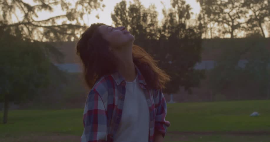 Woman with brown wavy hair and flannel shirt looks up and turns her head to camera in public park