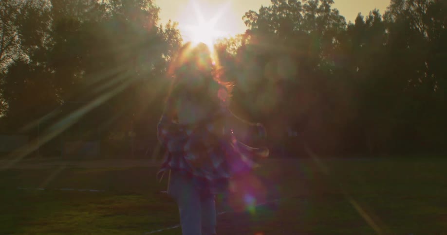 Woman runs across lawn toward trees as sun shines down