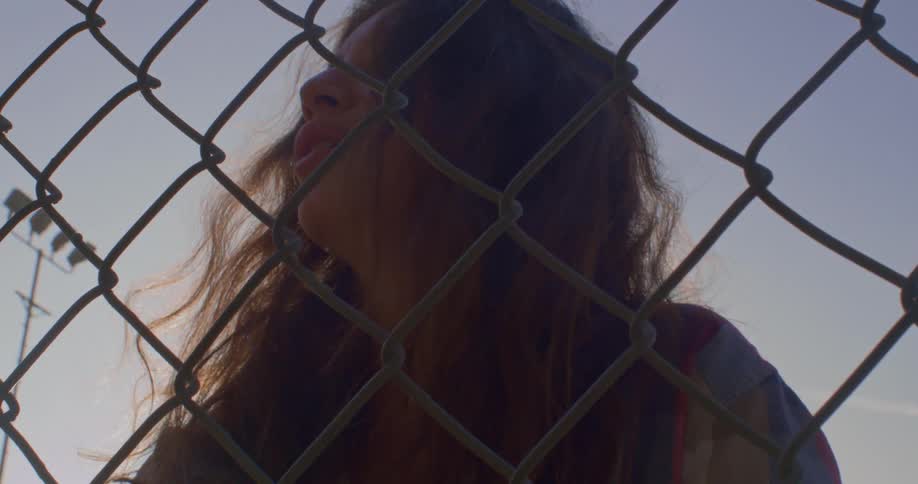 A woman poses behind a chain link fence