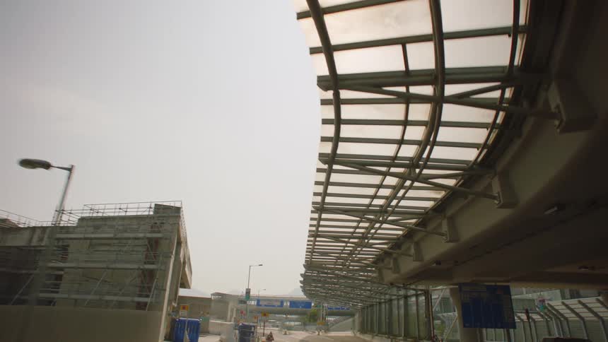 Vehicles sit in parking lot under overpass near skyscraper
