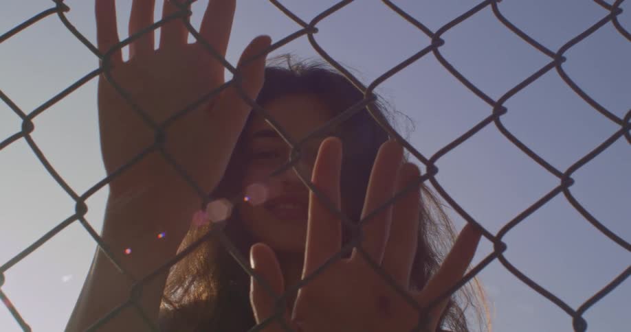 Woman with brown wavy hair touches chain link fence in park