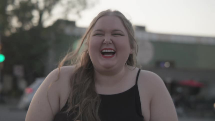 Young happy blonde woman smiles and laughs looking at the camera on the street of a town at sunset