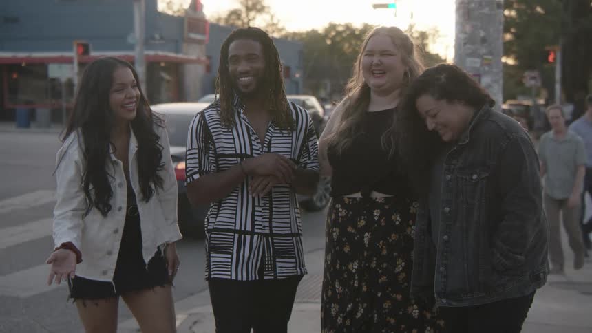 A group of people stand on the street corner laughing together