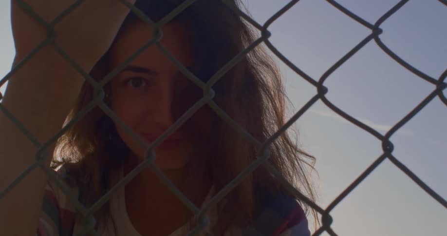 Woman leans forward smiling as she looks through chain link fence