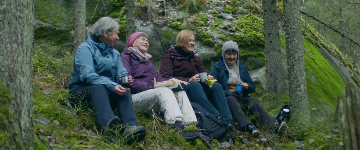 Group of elderly women eating food while sitting on the ground in the forest
