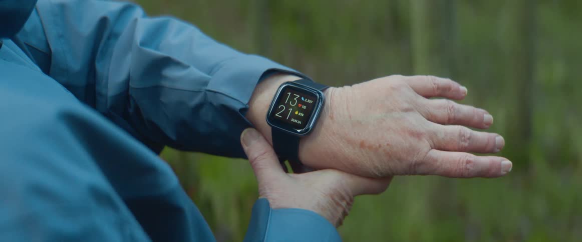 Elderly woman with blue jacket looks at smartwatch in the forest