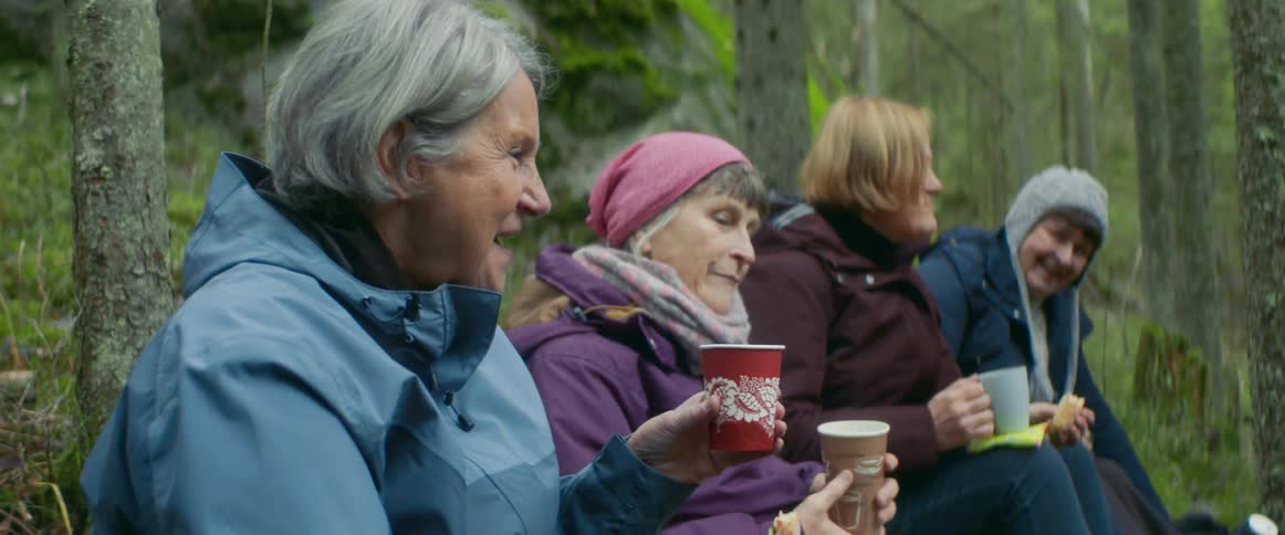 A group of women sitting outside surrounded by trees drinking coffee and talking