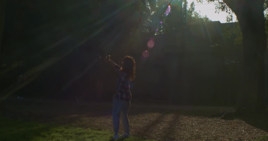Young woman holding a phone spins around on a park at sunset
