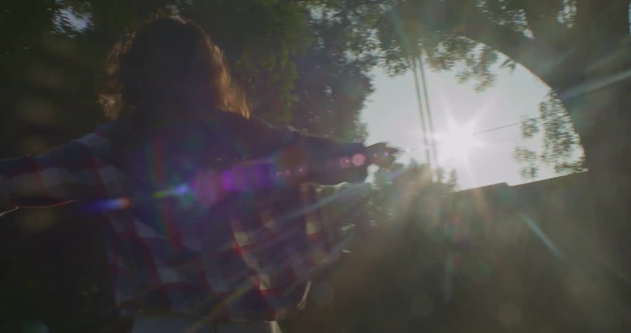 Woman stands outside in yard spinning with her arms spread wide as sun glares down
