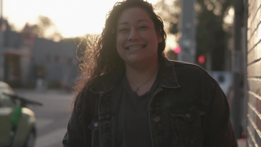 A woman who is standing outside in a town at sunset is smiling and laughing