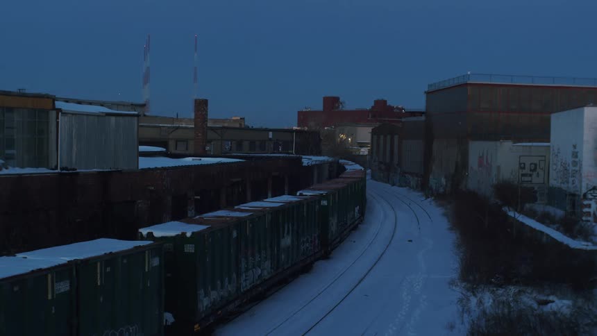 Train sits on track among snow near buildings decorated by graffiti