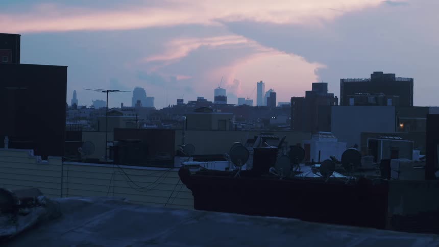 Several satellite dishes and antenna sit on rooftop with city skyline in the distance