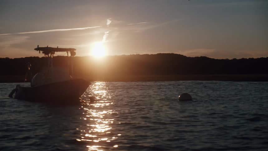 Buoy and boat floating over the surface of the ocean close to land at sunset