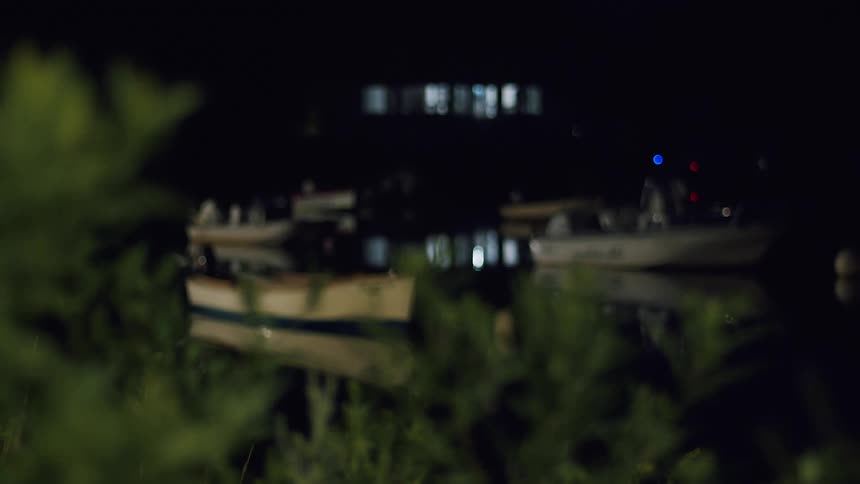 Boats sit near shore in calm reflective water at night