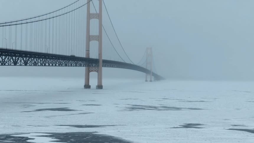 Car slowly crosses suspension bridge over frozen water on foggy day