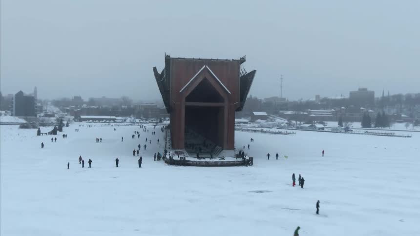 Aerial view of a bridge under construction over the frozen surface of a lake near a small city