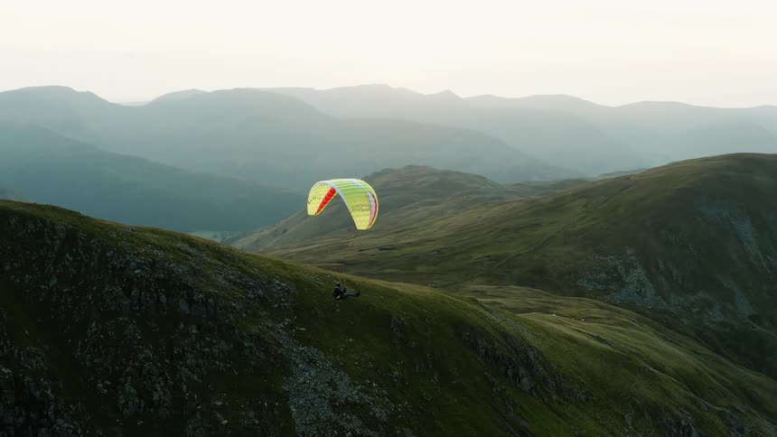 Aerial view of a person paragliding over a valley between the mountains at morning