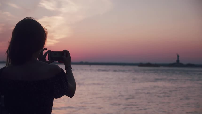 A woman is taking pictures of the sun setting above the ocean