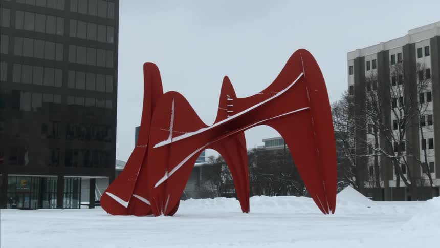 Abstract red metallic sculpture over the snow in a plaza between buildings