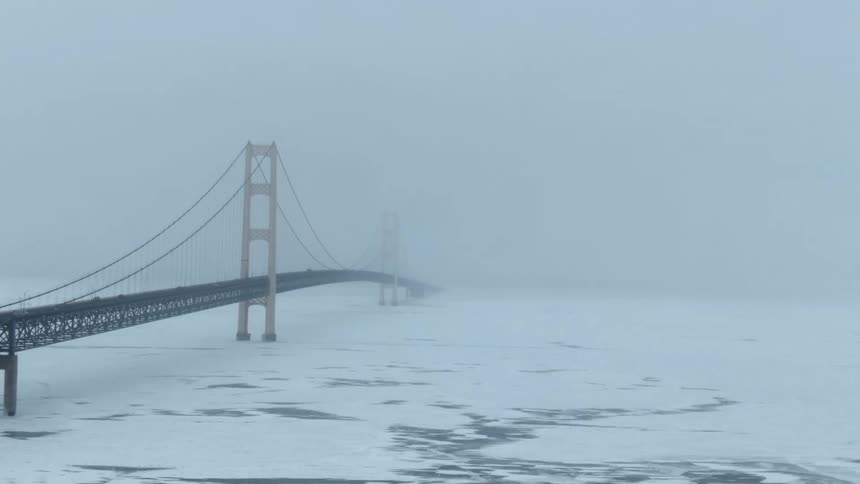Cars travel across a suspension bridge over snow and ice covered water
