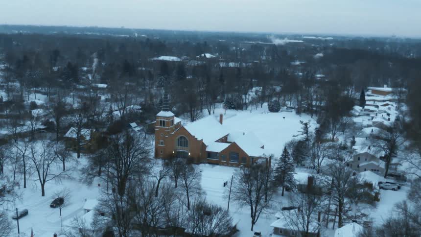 Vehicles drive along snow covered roads past church during winter
