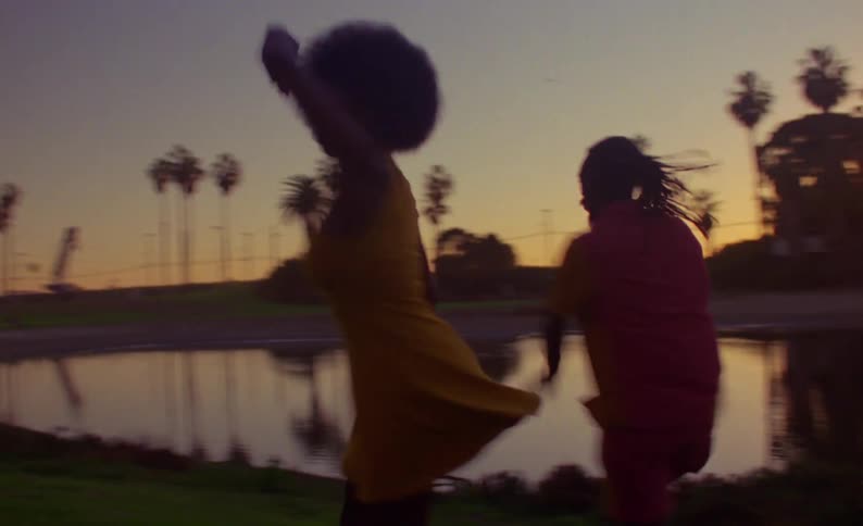 Dancers dance together on shore near pond at park under a red tinted sky