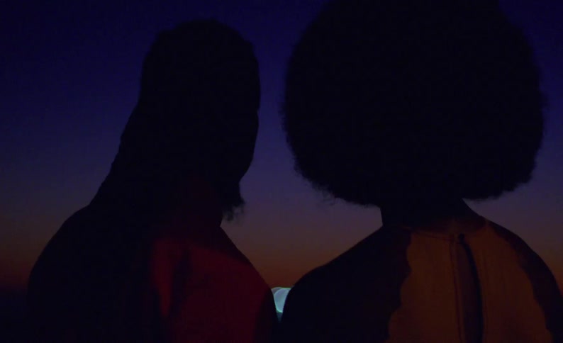 Man and woman stand outdoors at night looking toward remaining red glow on the horizon