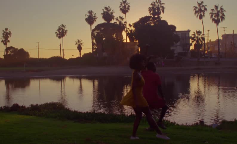 A man and woman dance on the shore in a tropical area as the sun sets