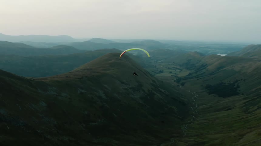 Aerial view of a person paragliding over a valley between the mountains in the evening