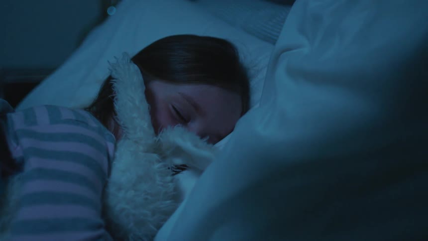 Young girl hugging a stuffed rabbit sleeping in the bed at home