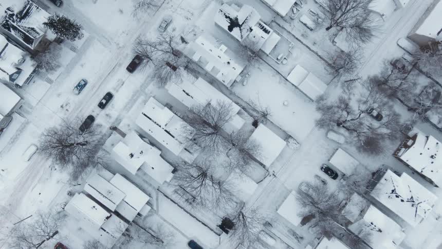 Top down aerial view of vehicles parked in a neighborhood with houses completely covered in snow