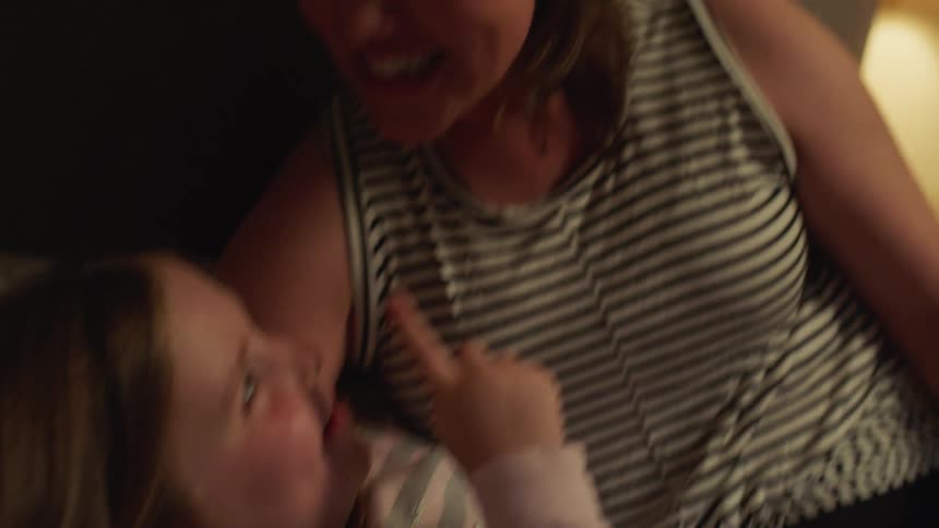 Mother puts her daughter to sleep with a story in the bedroom at home