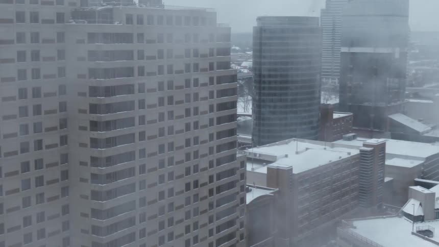 Drone breaks through white clouds revealing the skyline of a city covered in snow
