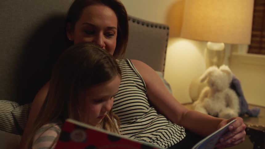 Mother reading her daughter a bedtime story in the bedroom at home