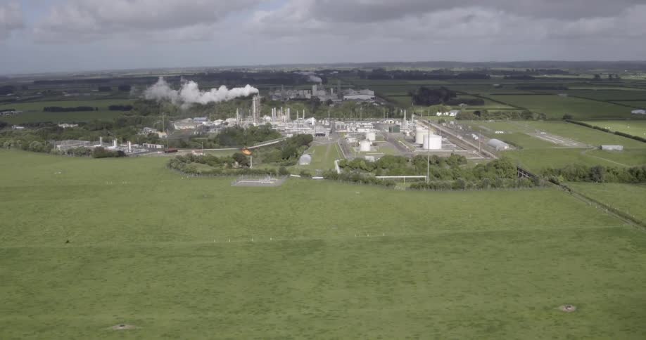 Aerial view of a grass field with some industrial buildings in the distance