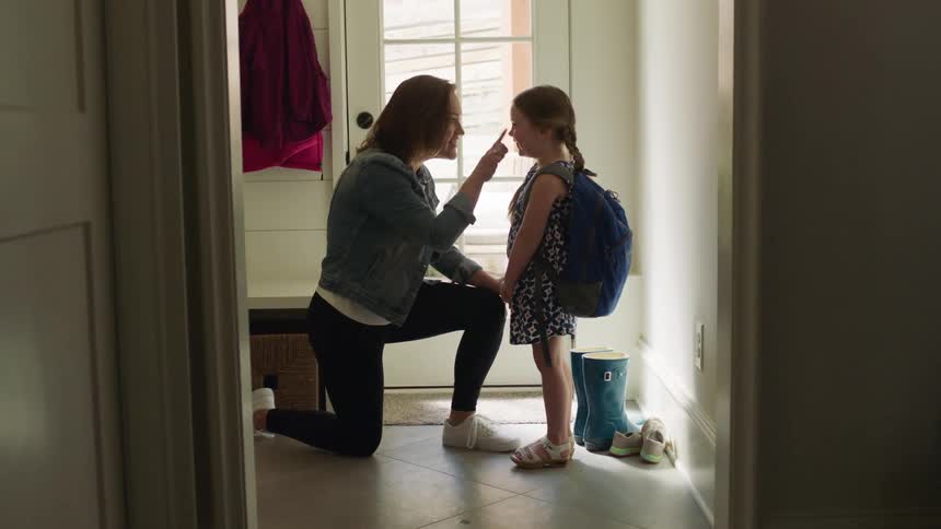 Mother checks on daughter standing near front door with a backpack