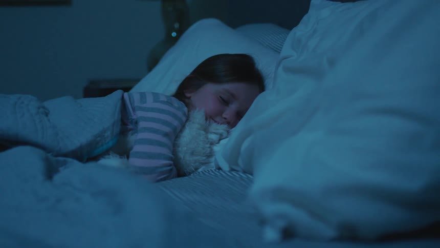 A young girl sleeps in a bed while hugging a plushy