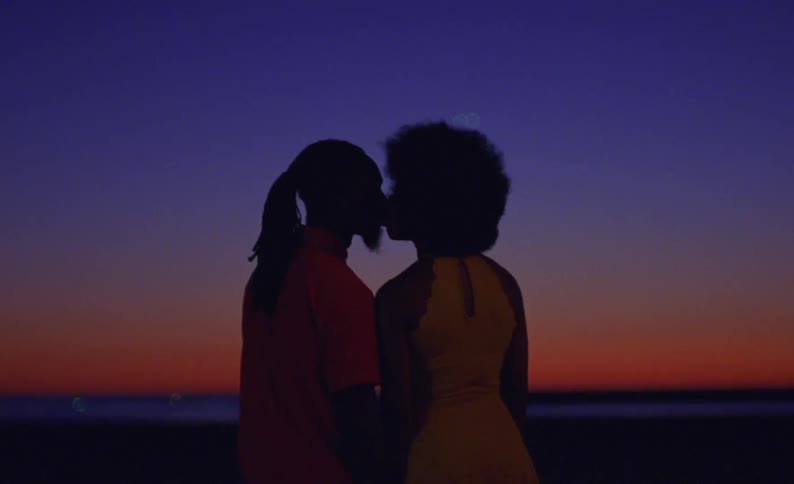Couple stand on beach facing red sky then kiss as airplane flies across night sky